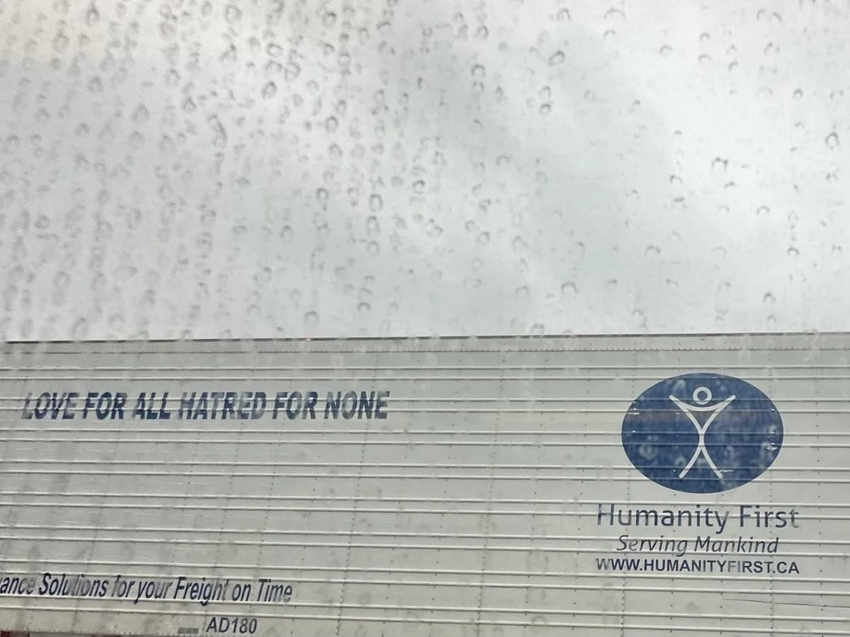 A view through a raindrop-covered window shows the side of a trailer featuring the slogan 'Love for all hatred for none' alongside the Humanity First logo.