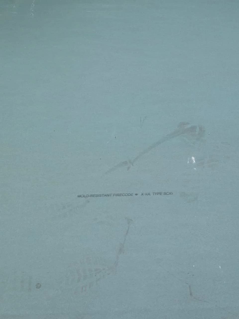 A pale greenish-blue mold-resistant drywall sheet features faint boot footprints and printed product text.
